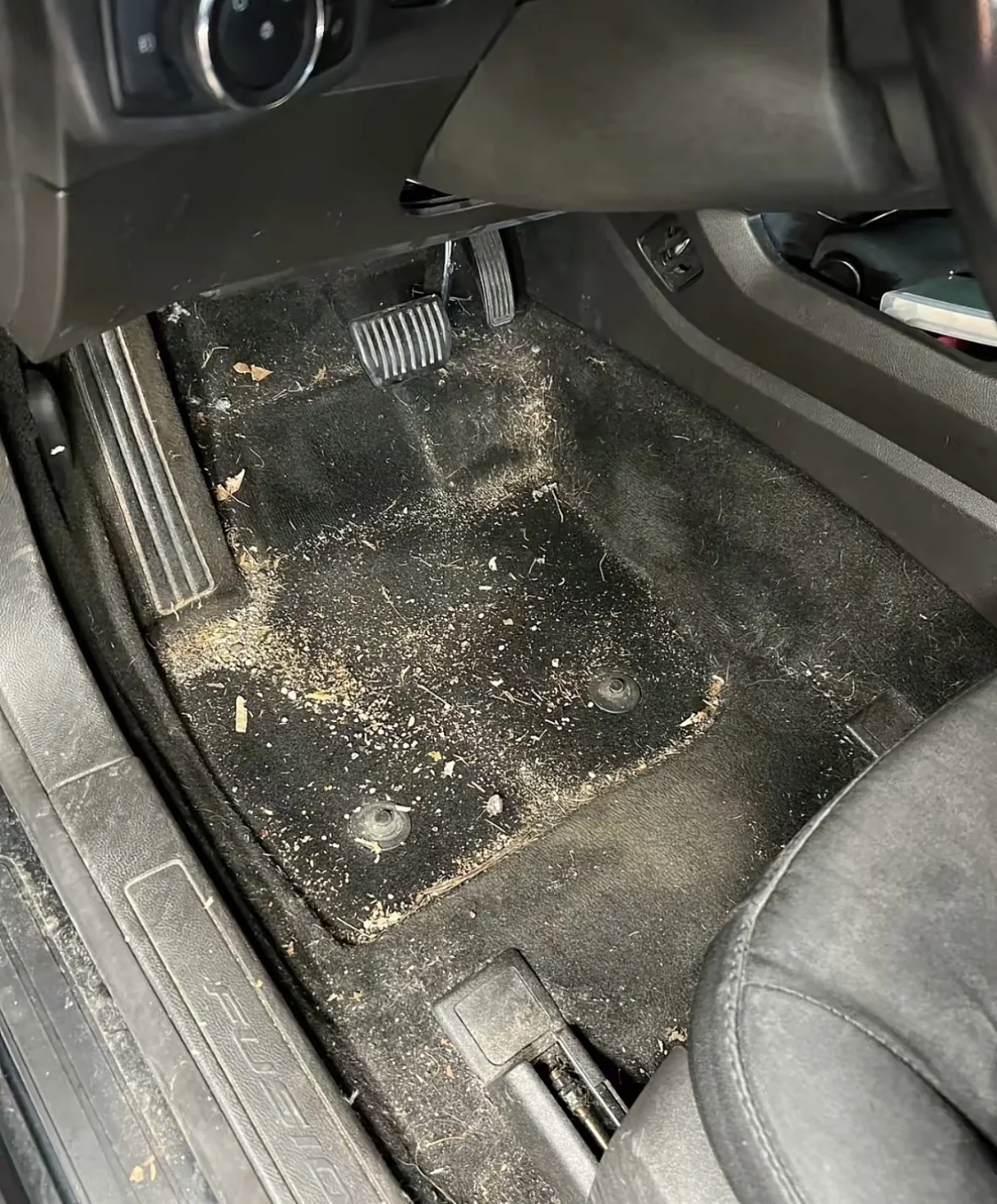Ford Fusion driver footwell before detailing, carpet covered in dirt and debris